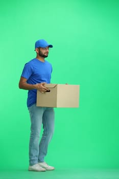 A male deliveryman, on a green background, full-length, with a box.