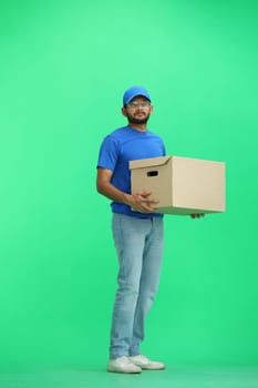 A male deliveryman, on a green background, full-length, with a box.