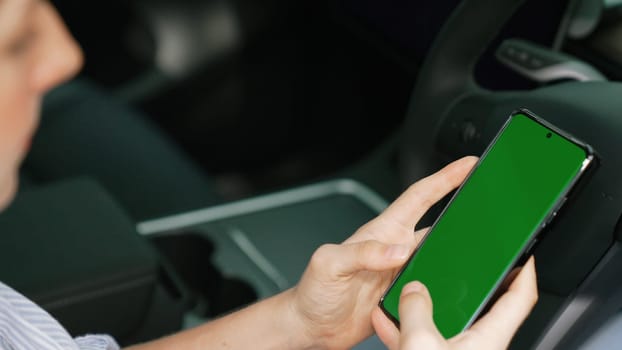 Holiday vacation road trip with environmental-friendly car concept. Eco-conscious woman on driver seat holding blank copyspace green screen smartphone for EV battery status. Exalt