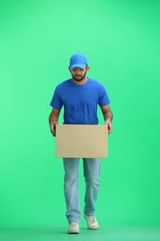 A male deliveryman, on a green background, in full height, puts a box.