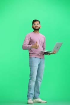 A man, on a green background, in full height, uses a laptop.