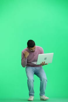 A man, on a green background, in full height, uses a laptop.
