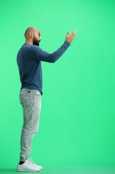 A man, on a green background, in full height, calls to himself.