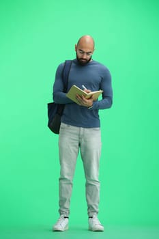 A man, on a green background, in full height, writes.
