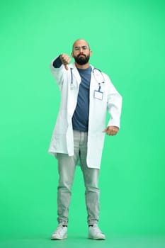 A male doctor, on a green background, in full height, shows his thumbs down.