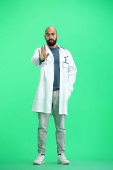 A male doctor, on a green background, in full height, shows a stop sign.