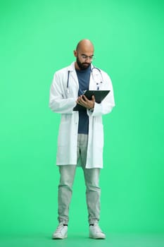 A male doctor, on a green background, in full height, writes.