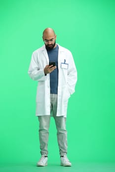 Male doctor, on a green background, full-length, with a phone.