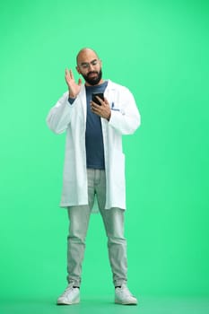 Male doctor, on a green background, full-length, with a phone.
