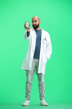 Male doctor, on a green background, full-length, with a phone.