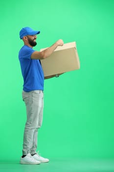 A male deliveryman, on a green background, in full height, points to the box.