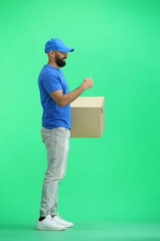 A male deliveryman, on a green background, in full height, with a box, shows a stop sign.