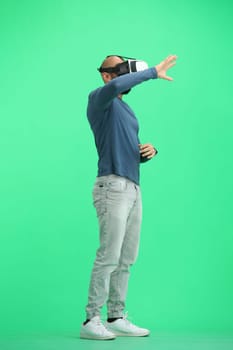 Man, on a green background, full-length, wearing VR glasses.