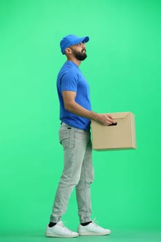 A male deliveryman, on a green background, full-length, with a box.