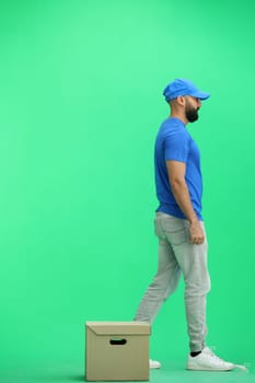 A male deliveryman, on a green background, in full height, puts a box.