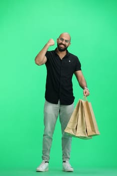 A man, on a green background, full-length, with bags, raised his hand up.