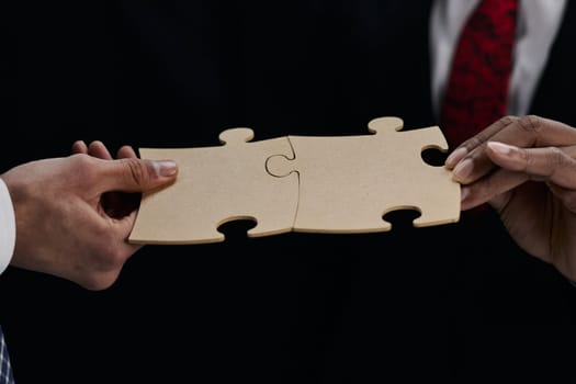 Close-up Of Business Partners Combining Two White Puzzle Pieces On Black Background