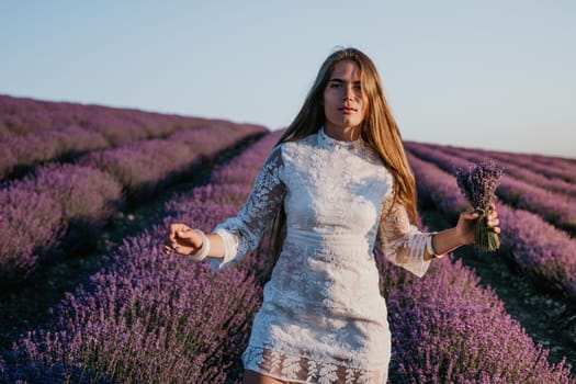 Close up portrait of young beautiful woman in a white dress and a hat is walking in the lavender field and smelling lavender bouquet.