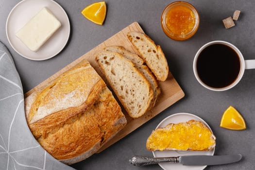 Cup of coffee, sandwich with orange jam, loaf of bread on the grey background. Breakfast concept.