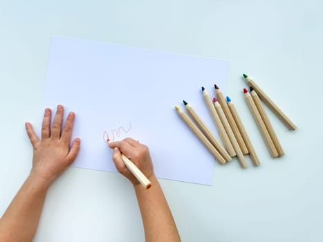 small child draws with colored pencils on paper on white table. High quality photo