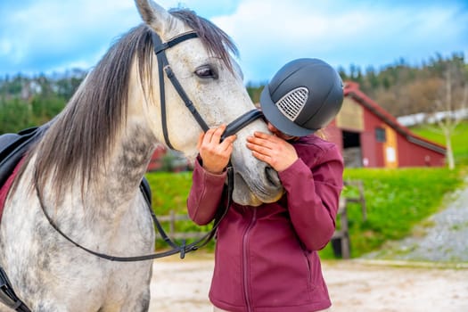 Woman kissing a horse in the noise standing outside an equestrian center