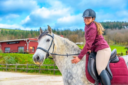 Happy young woman riding a white horse in an equestrian center