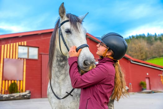 Female young jockey with helmet caressing a horse head on a equestrian center