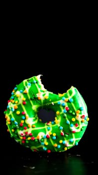 Green glazed donut with sprinkles isolated. Close up of colorful bitten donut.