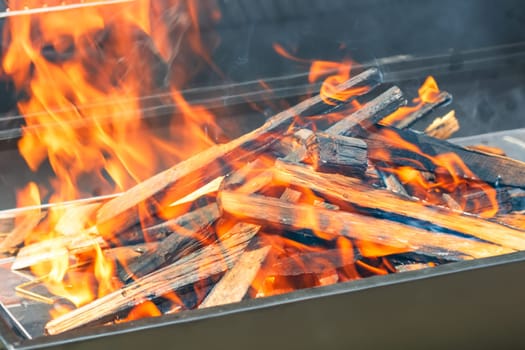 Barbecue grill pit with glowing and flaming hot open fire with red flame, hot charcoal briquettes and embers