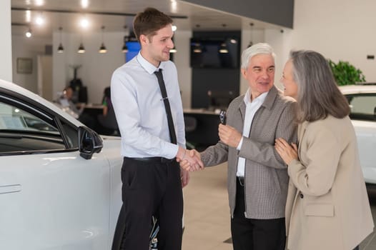 A salesman hands over the keys to a new car to an elderly Caucasian couple