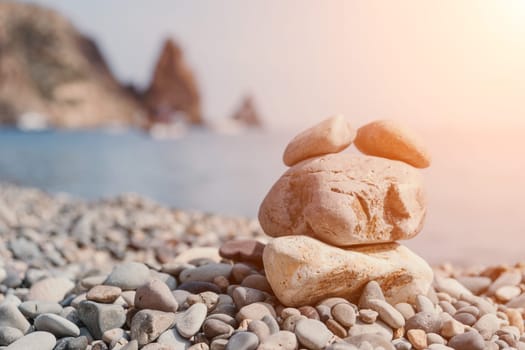 Pyramid stones on the seashore with warm sunset on the sea background. Happy holidays. Pebble beach, calm sea, travel destination. Concept of happy vacation on the sea, meditation, spa, calmness.