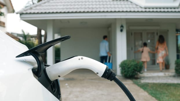 Happy family return from holiday and travel while recharging electric EV car's battery at home charging station. EV car and modern family concept. Synchronos