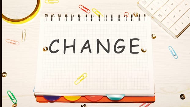CHANGE word on a checkered notebook on a light table next to a magnifying glass, paper clips, stationery buttons, a calculator
