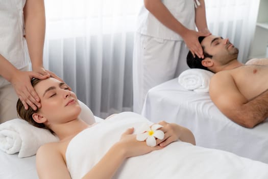 Caucasian couple enjoying relaxing anti-stress head massage and pampering facial beauty skin recreation leisure in dayspa modern light ambient at luxury resort or hotel spa salon. Quiescent