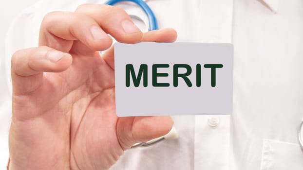 Merit word on the card in a man's hand on the background of a white shirt