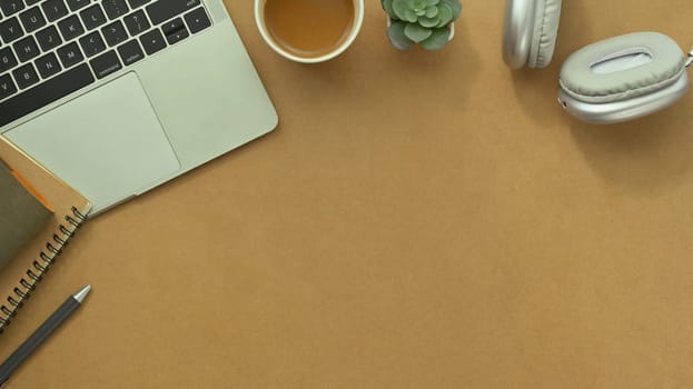 Laptop, cup of coffee, notepad and headphone on brown background. Top view with copy space.