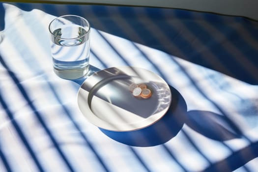 Photo of a medicine pills in a dish and glass of water with condensation.
