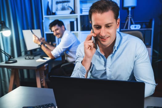 Serious businessman calling on phone with customer to create new project at night time, coworker writing document work sheet on desk. Concept of working on neon blue light modern office. Sellable.