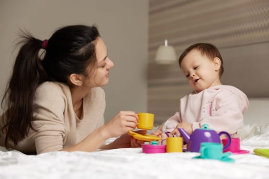 happy mother and little child daughter pretending drinking tea from toy cups and spending time together in bedroom, family having fun