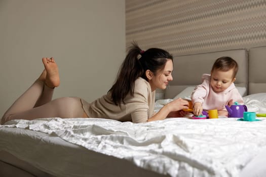 happy mother and little child daughter playing tea party and spending time together on bed