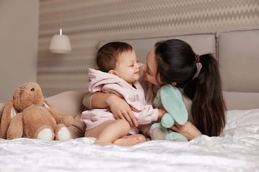 happy mother and her little child daughter playing with bunny toys in bedroom, family having fun