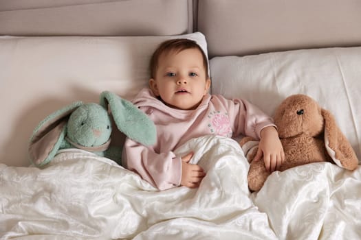 cute little child with fluffy toy bunny in white bed