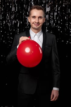 caucasian man in black jacket with red air balloon on dark glitter background. birthday party