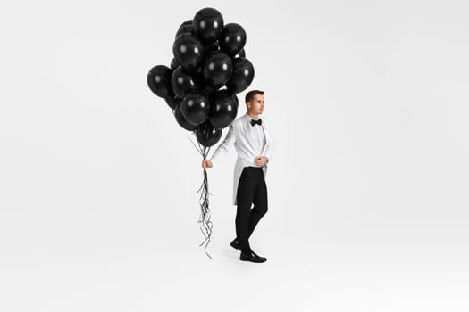 elegant caucasian businessman in white suit tuxedo holding helium ballons on white background.