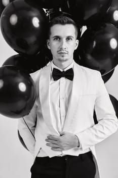 elegant caucasian man in white suit tuxedo with black air balloons on white background.