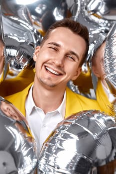 portrait of happy man in yellow jacket with a lot of silver air balloons. birthday party