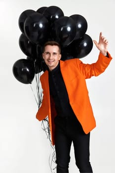 smiling man in orange jacket with black air balloons on white background. birthday party