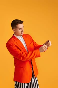 Cheerful funny young man in orange jacket and striped pants on yellow background.