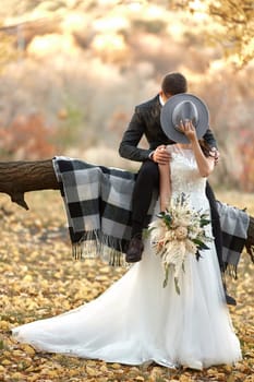beautiful happy stylish bride and groom kissing and covering by hat outdoor in autumn