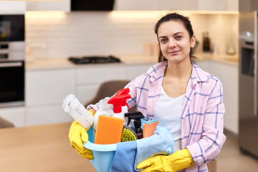 Woman in rubber protective yellow gloves holding bucket with cleaning detergents and rags . house chores.